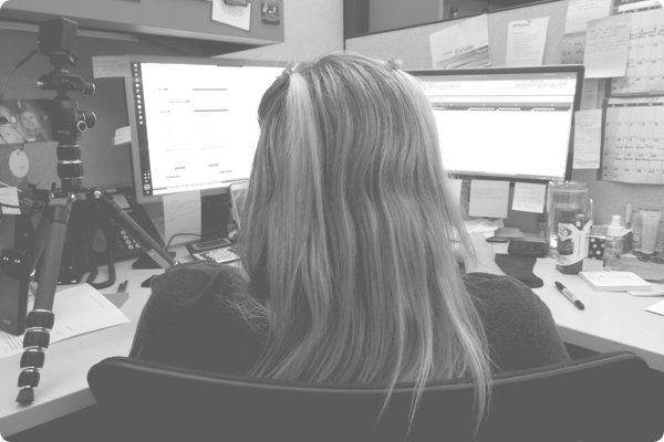 An office manager sitting at her desk looking at two monitors attempting to place a print order online.