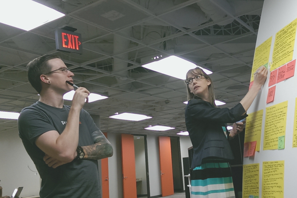 A man and woman standing in front of a post it note covered display board