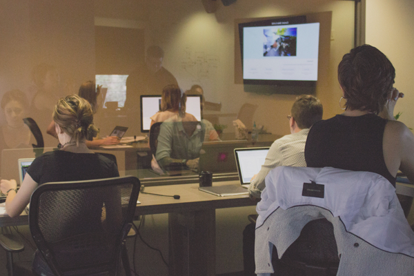 Multiple individuals sitting inside a user testing lab observing a participant