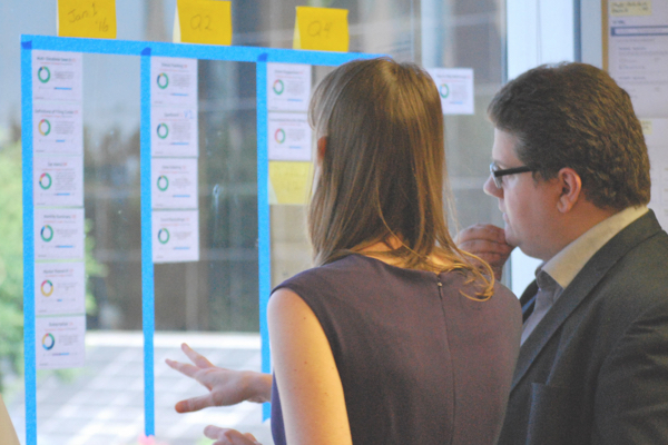 Woman speaking to a man pointing at a glass window covered in sticky notes